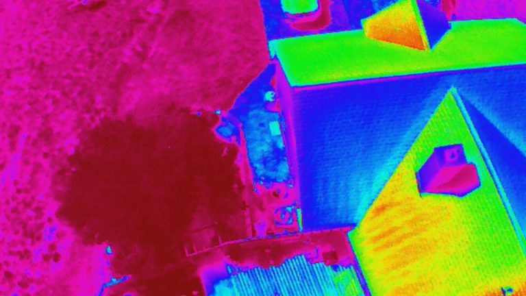 Infrared aerial view of a house with a vivid color scale. Roof shows heat variations in yellow and blue. Surrounding yard is magenta.
