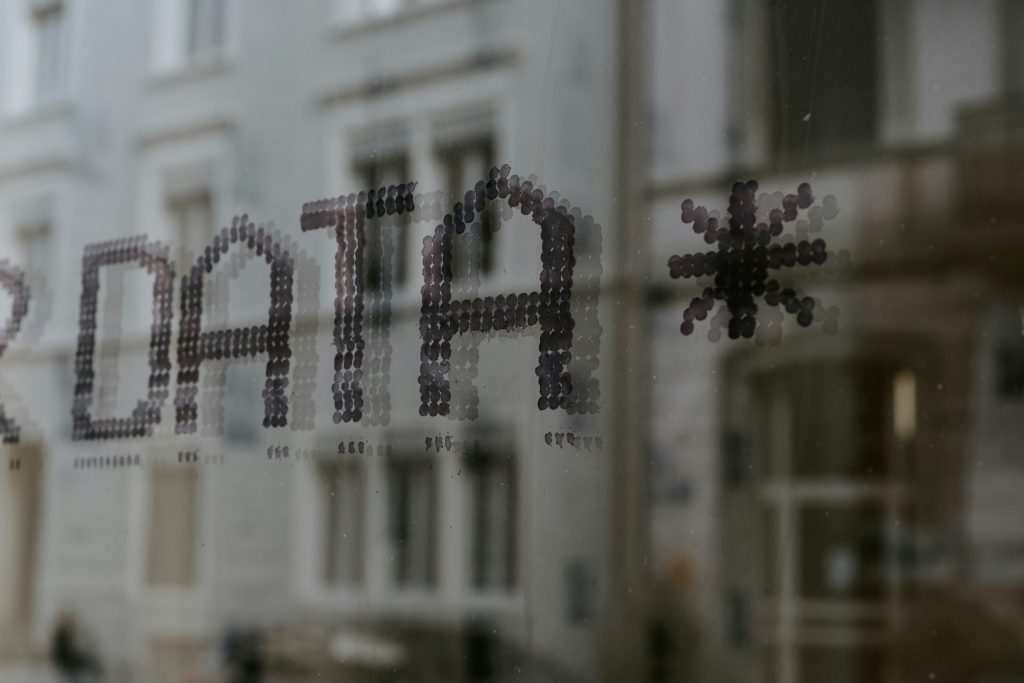 Text "DATA" in dotted style on a window, reflecting a gray urban building backdrop. Textured, moody, with a subtle geometric design.