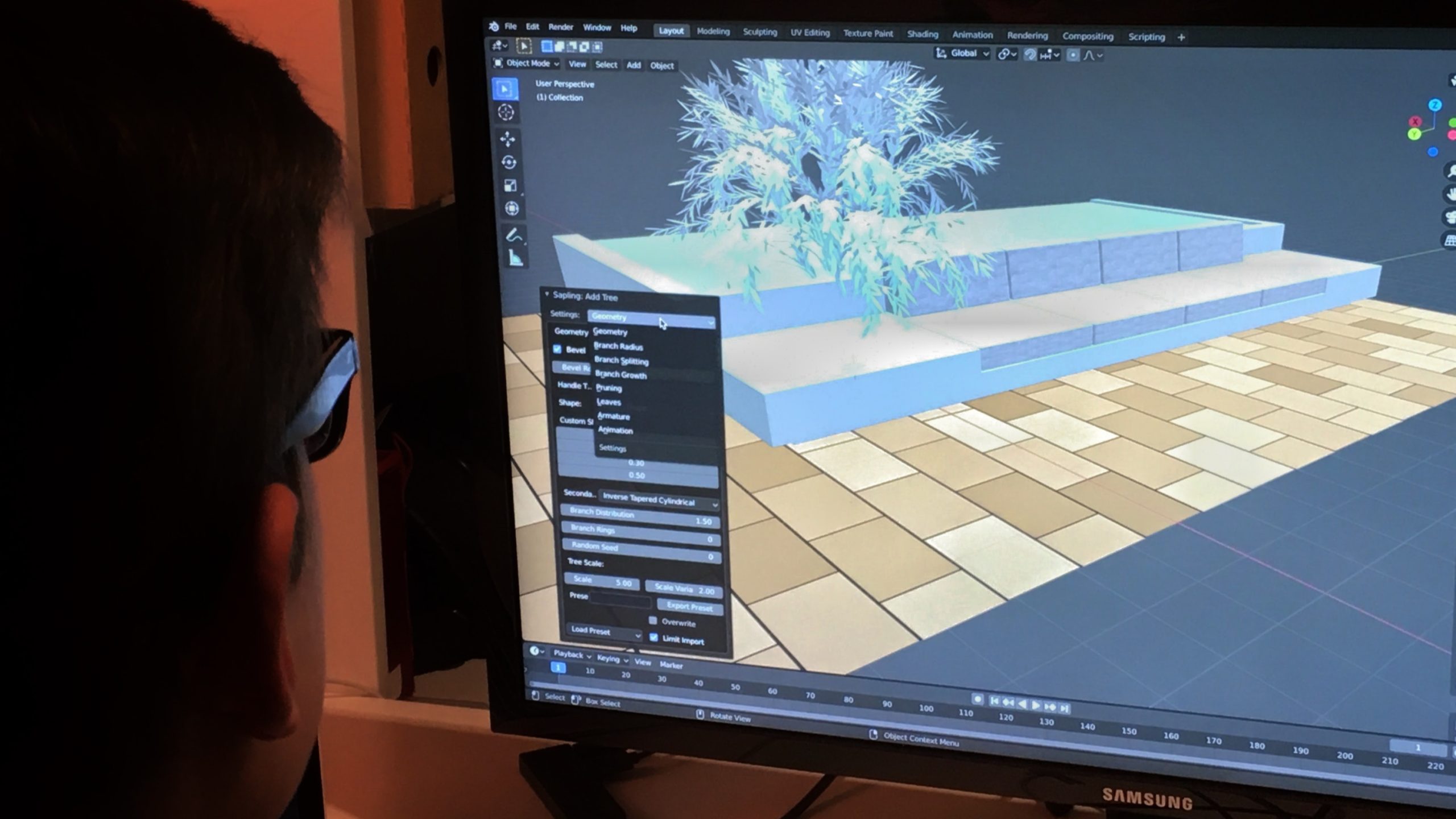 Person working on 3D tree design in software on a Samsung monitor. The screen shows a digital platform and trees with menu options visible.