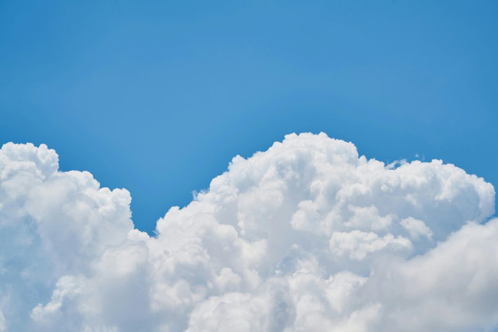 Fluffy white clouds against a bright blue sky, evoking a sense of tranquility and openness. The scene is calm and serene, with soft textures.