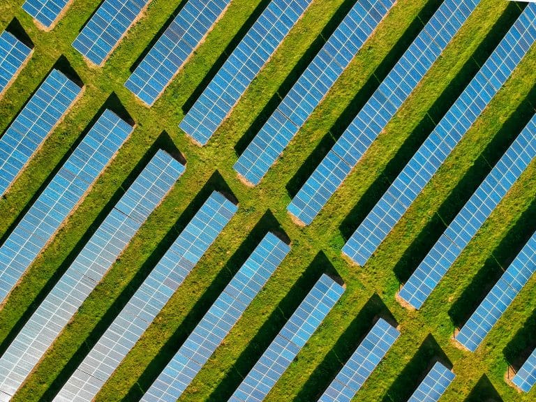 Aerial view of rows of solar panels on green grass, forming a geometric pattern. Panels are aligned diagonally, conveying a sense of order and sustainability.
